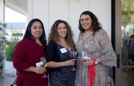 Three women enjoy a glass of wine at a social